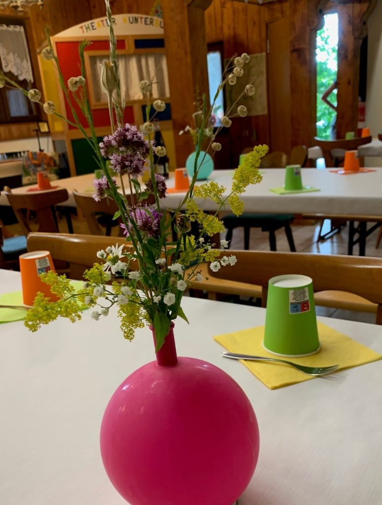 Pinker Luftballon mit Wiesenblumenstrauß auf einem Tisch mit bunten Bechern und Servietten
